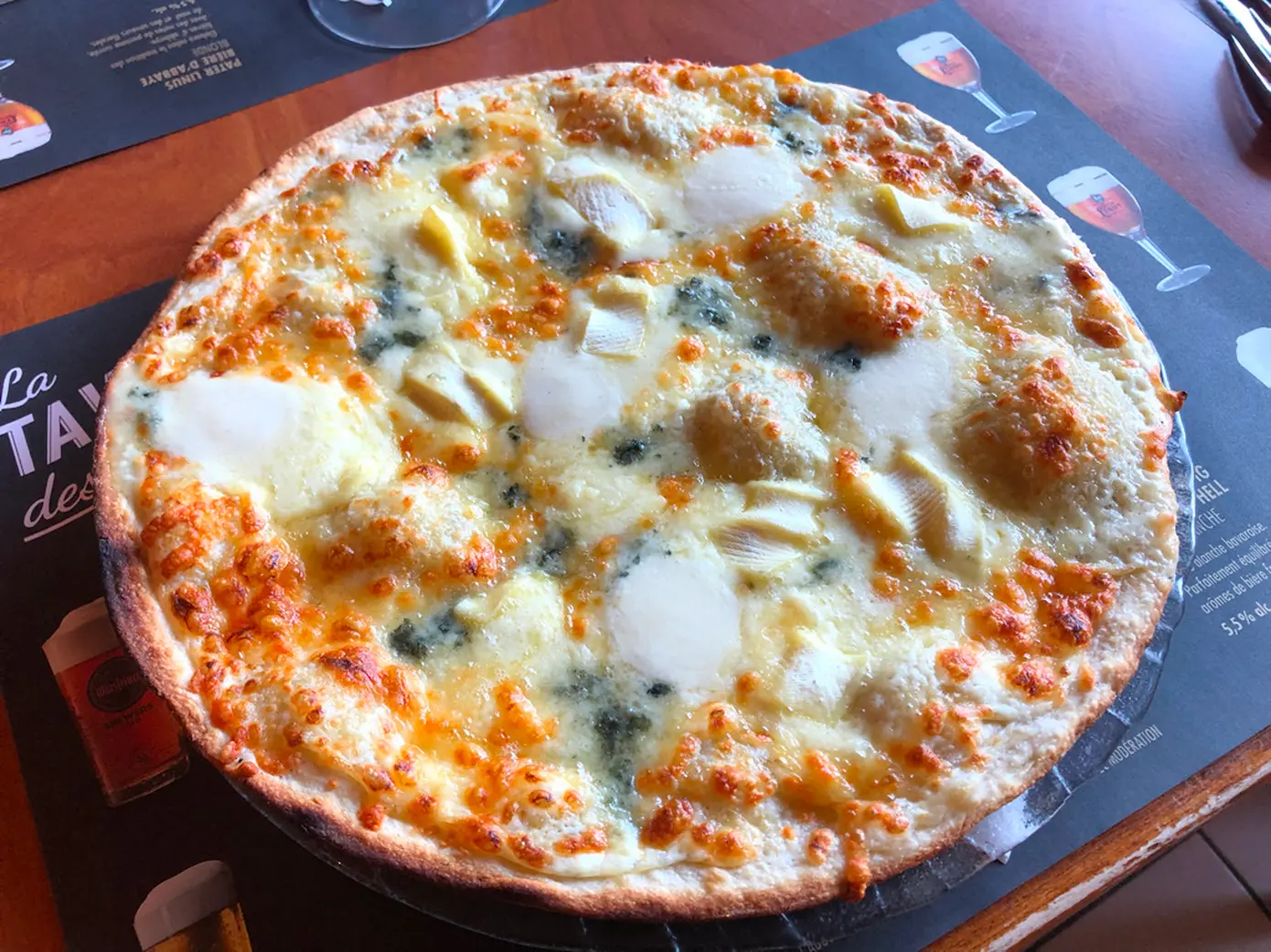 Pizza gratinée au fromage servie sur un set de table La Taverne