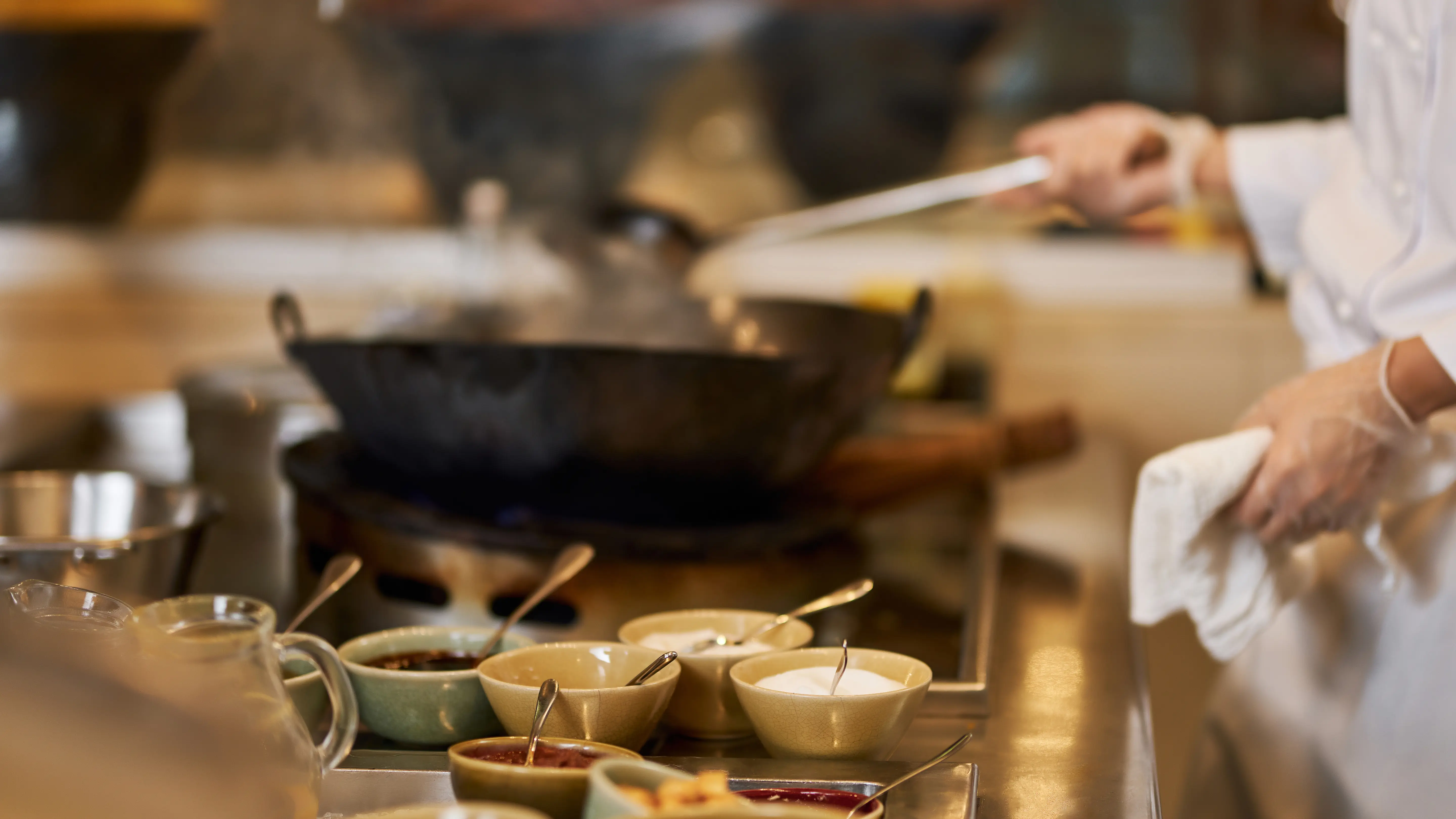 Cuisinier préparant un plat au wok en cuisine, entouré de bols de sauces