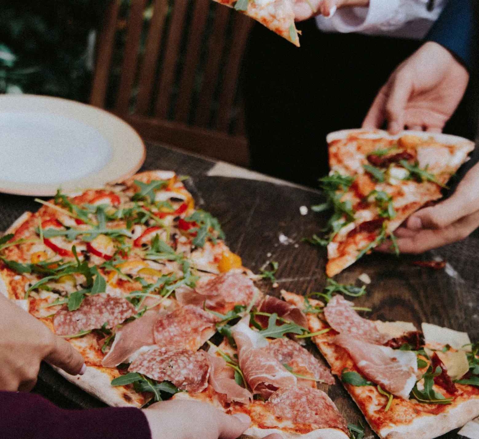Pizza à la charcuterie et roquette partagée entre convives à table